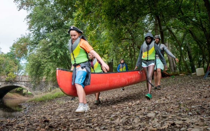 a group of teens carry a canoe to water on an outward bound expedition 